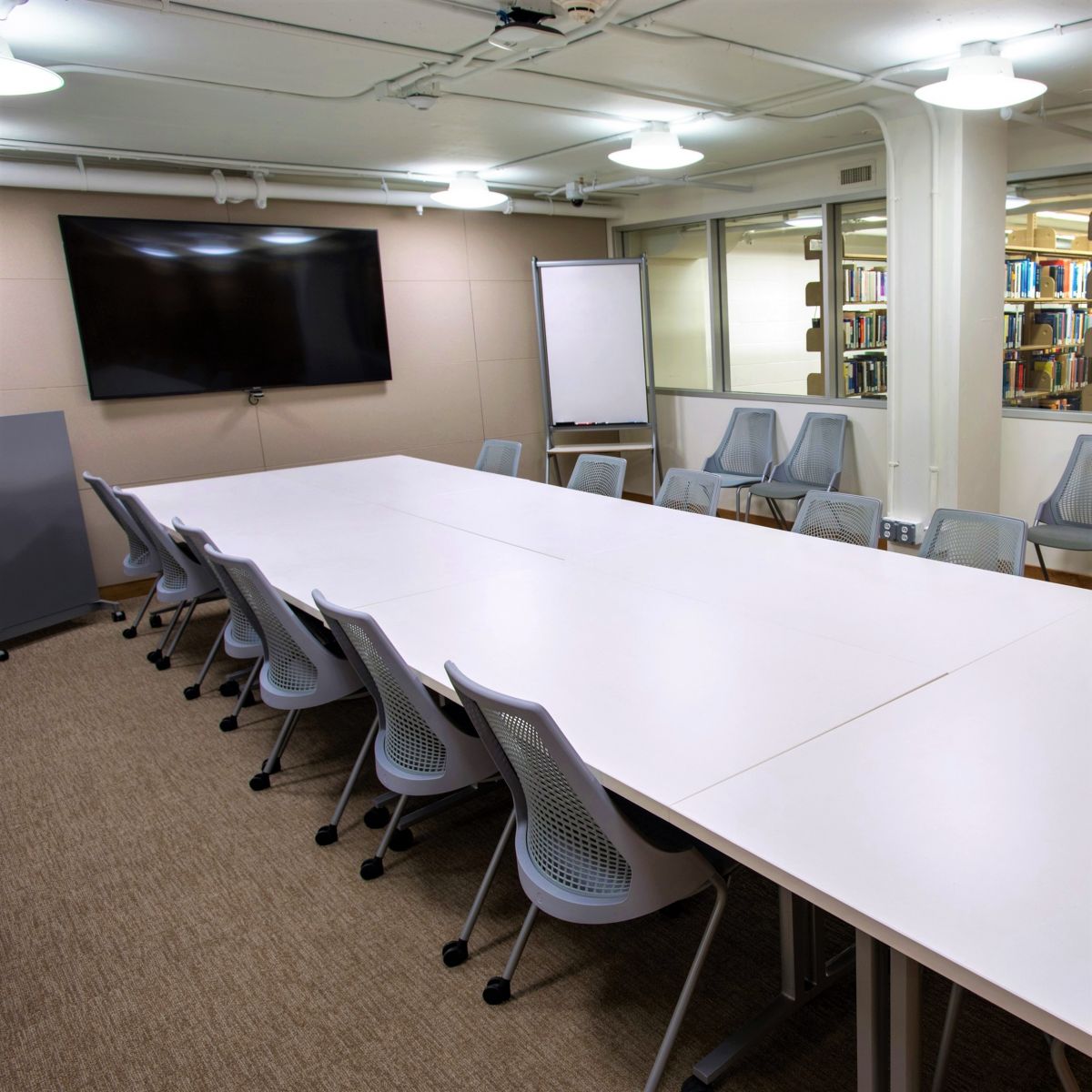 Image of the lower level seminar room in Marx Library. Also referred to as S57. Image features a large conference table with twelve chairs and wall monitor. 